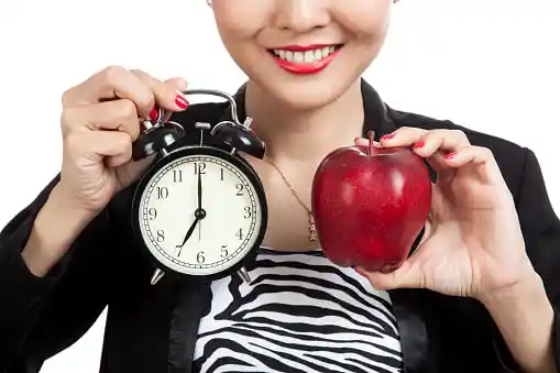 young woman holding an alarm clock in one hand and an apple in the other