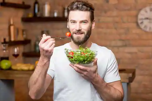 young man ready to take a bite from the bowl of green salad leaves he is holding