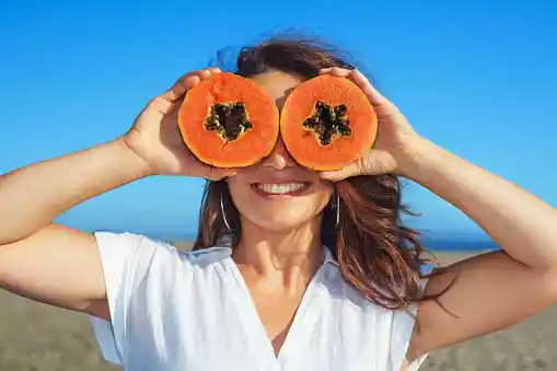  woman holding papaya slices over eyes=